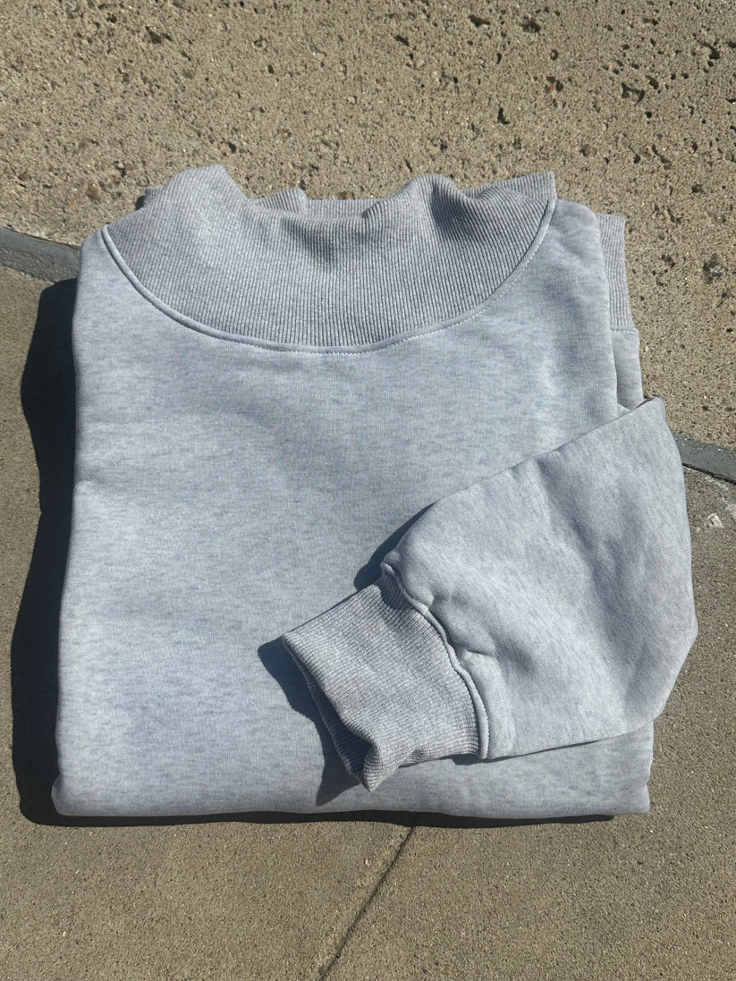 A light gray heather crewneck sweatshirt laid flat on a concrete surface.