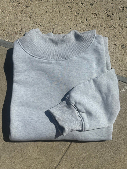 A light gray heather crewneck sweatshirt laid flat on a concrete surface.