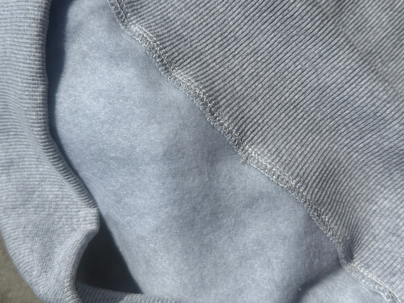 Close-up of a light gray ribbed knit fabric meeting a smoother light gray fleece or microfiber lining, showing the texture and stitching detail of the offered mock neck sweatshirt.