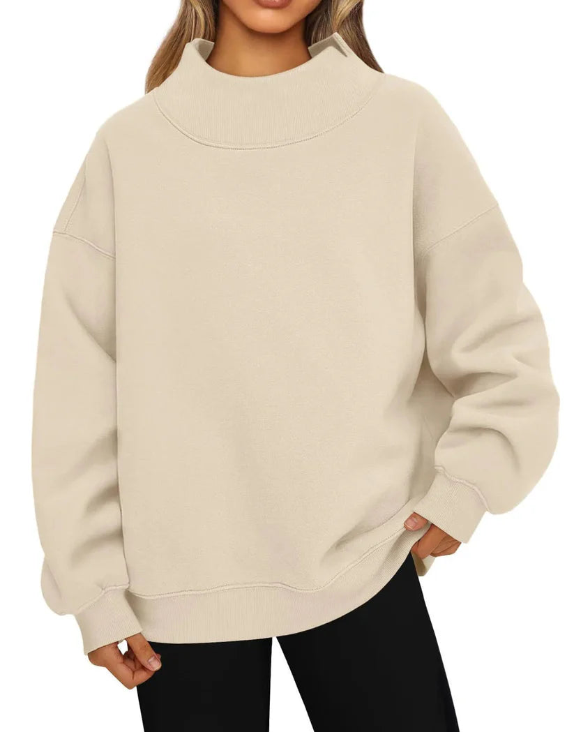 A woman wearing an oversized apricot (cream-colored) mock neck sweatshirt with black pants, shown from the chin down against a plain white background.